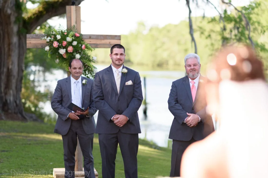Groom waits at the wooden cross altar by the Waccamaw River as the bride approaches at Upper Mill Plantation