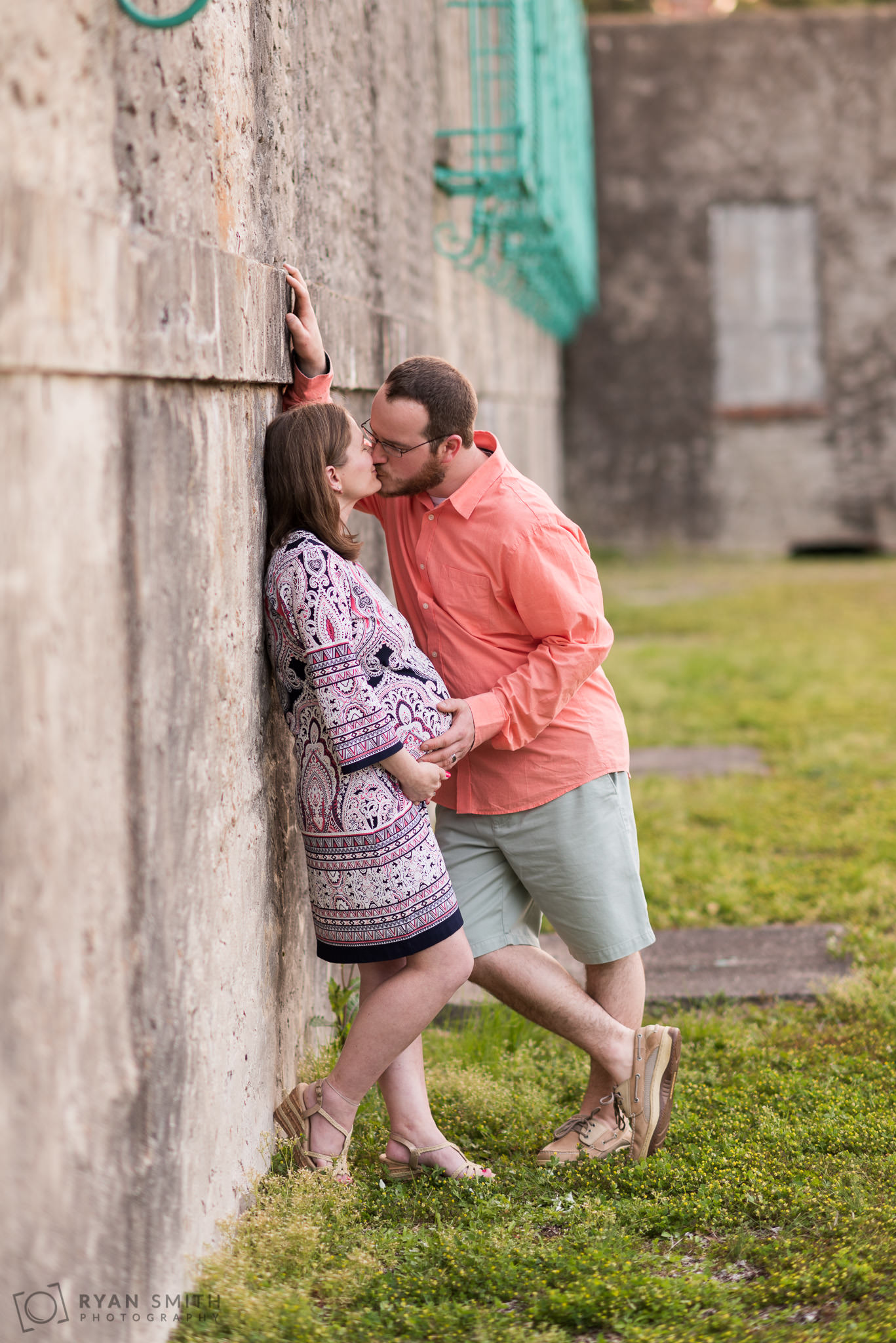 Man kissing expecting wife by the castle wall Huntington Beach State Park