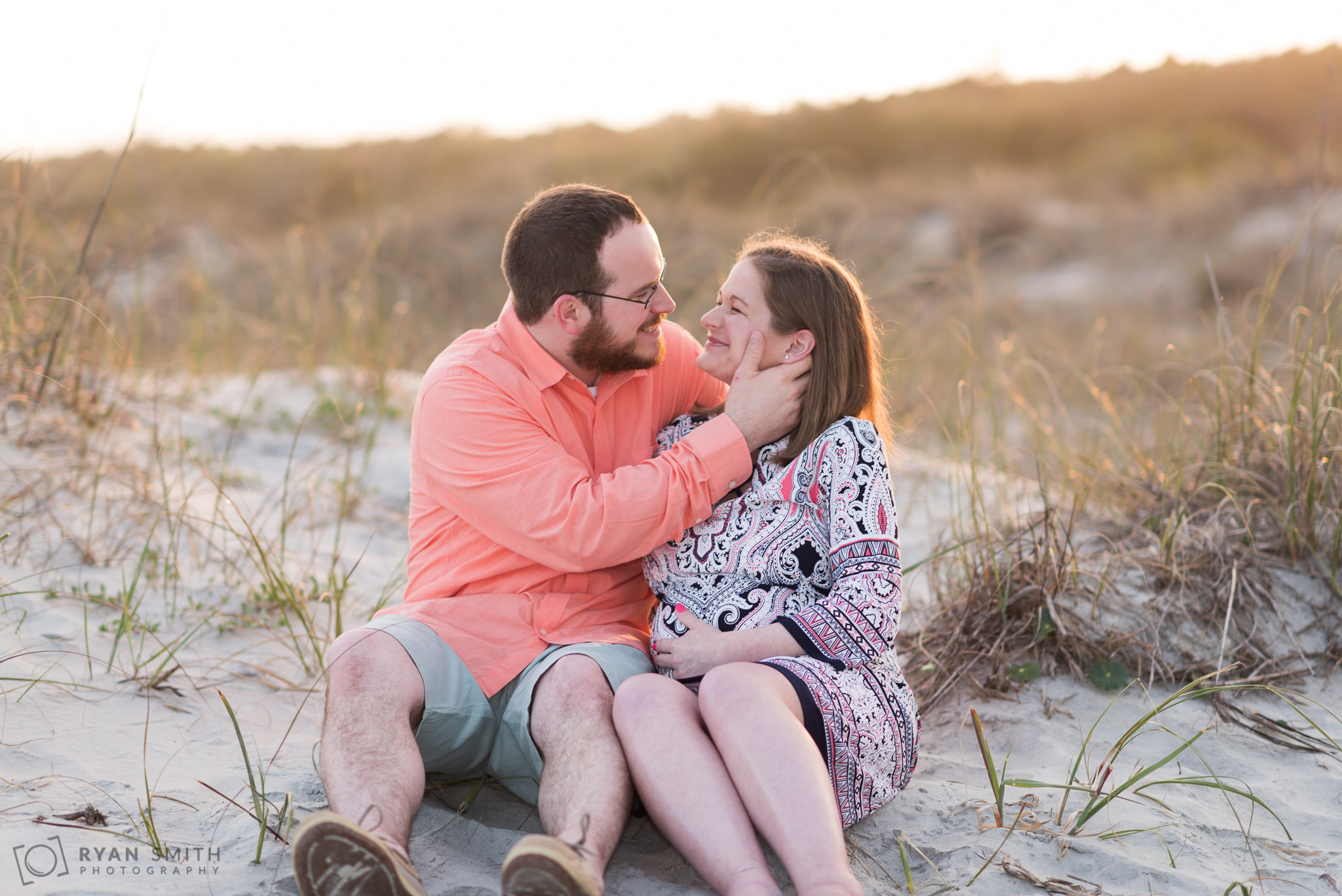 Maternity portraits of man and woman sitting by the dunes Huntington Beach State Park