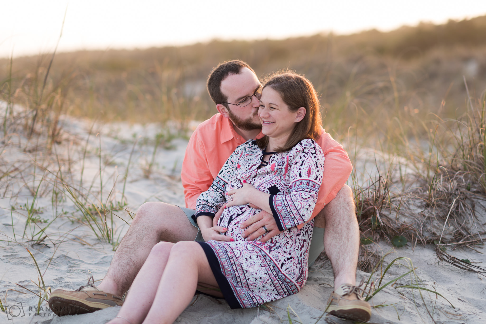 Maternity portraits of man and woman sitting by the dunes Huntington Beach State Park