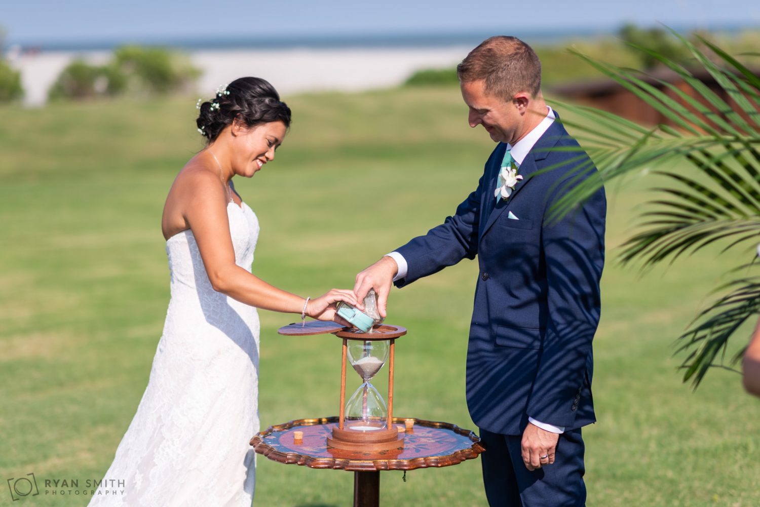 Bride and groom putting sand into an hourglass Dunes Golf and Beach Club