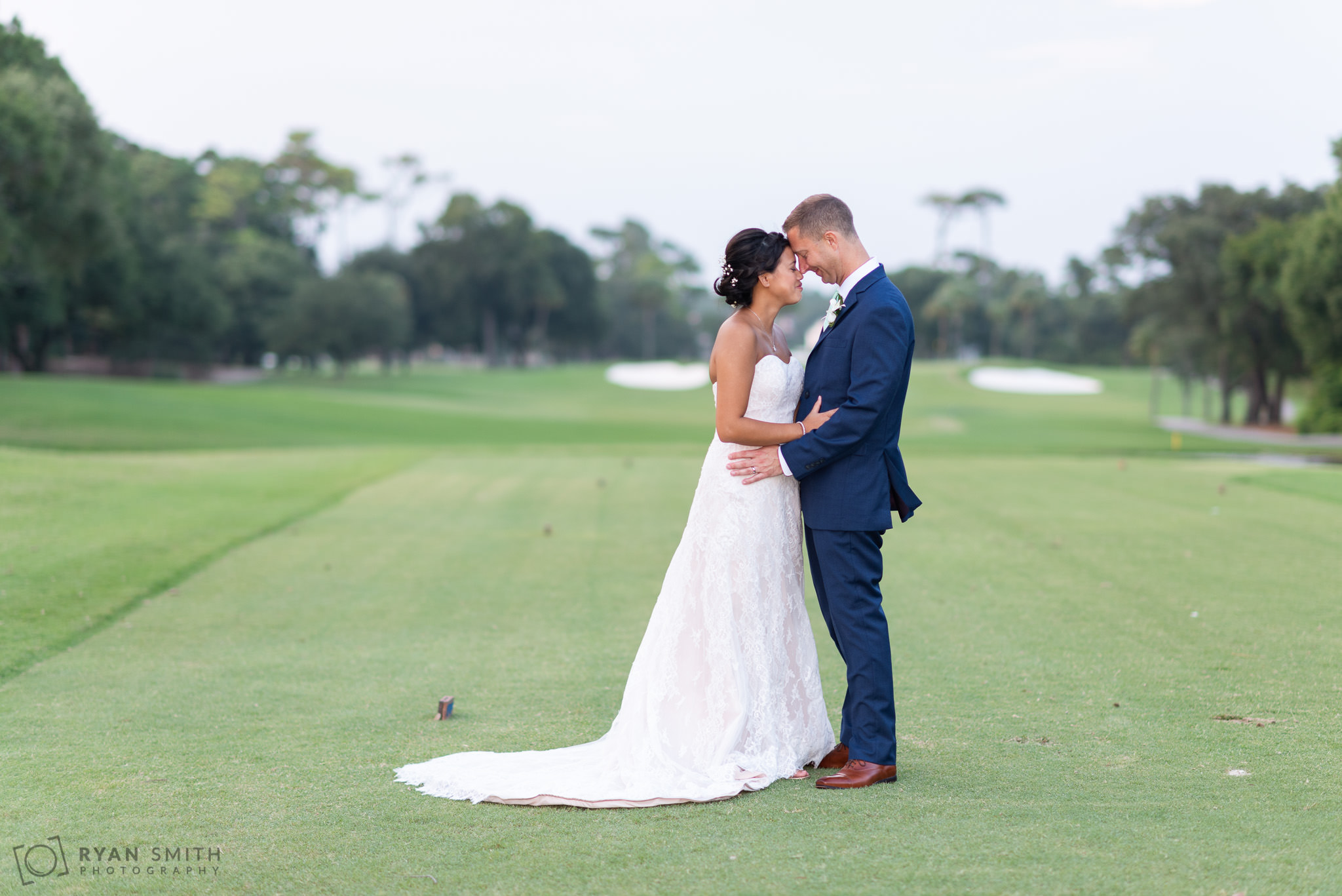 Bride and groom touching noses on the golf course Dunes Golf and Beach Club