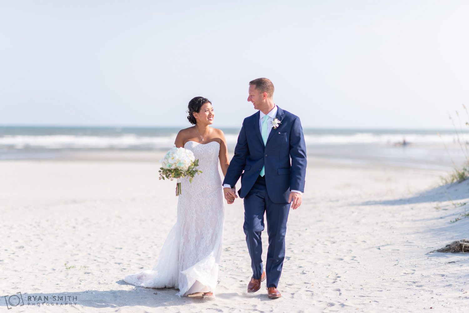 Bride and groom walking down the beach Dunes Golf and Beach Club