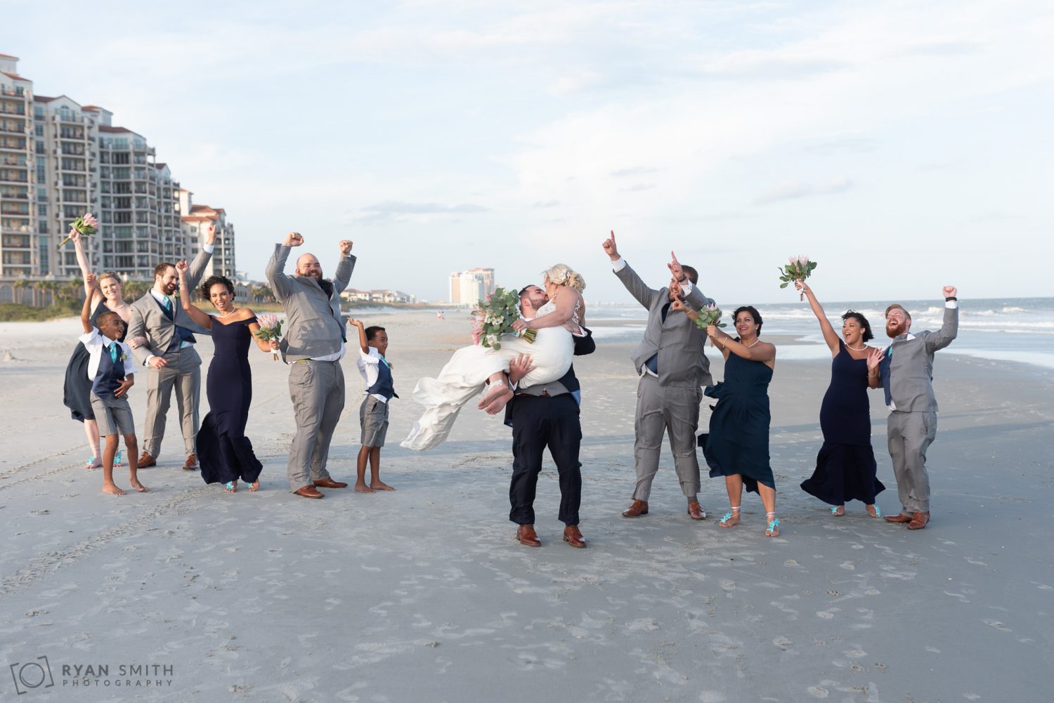Groom lifting up the bride for a kiss with bridal party cheering Grande Dunes Ocean Club