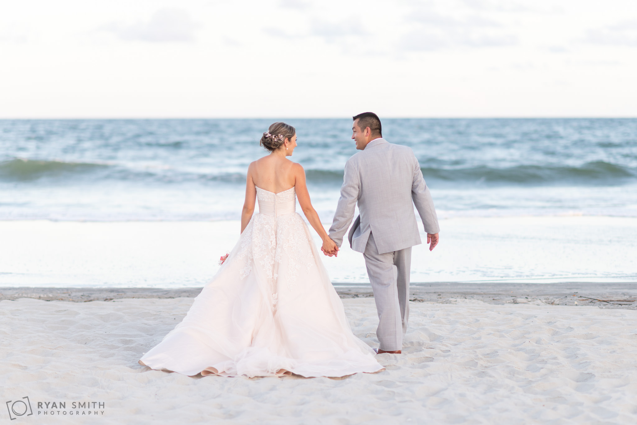 Bride and groom walking towards the ocean holding hands Grande Dunes Ocean Club