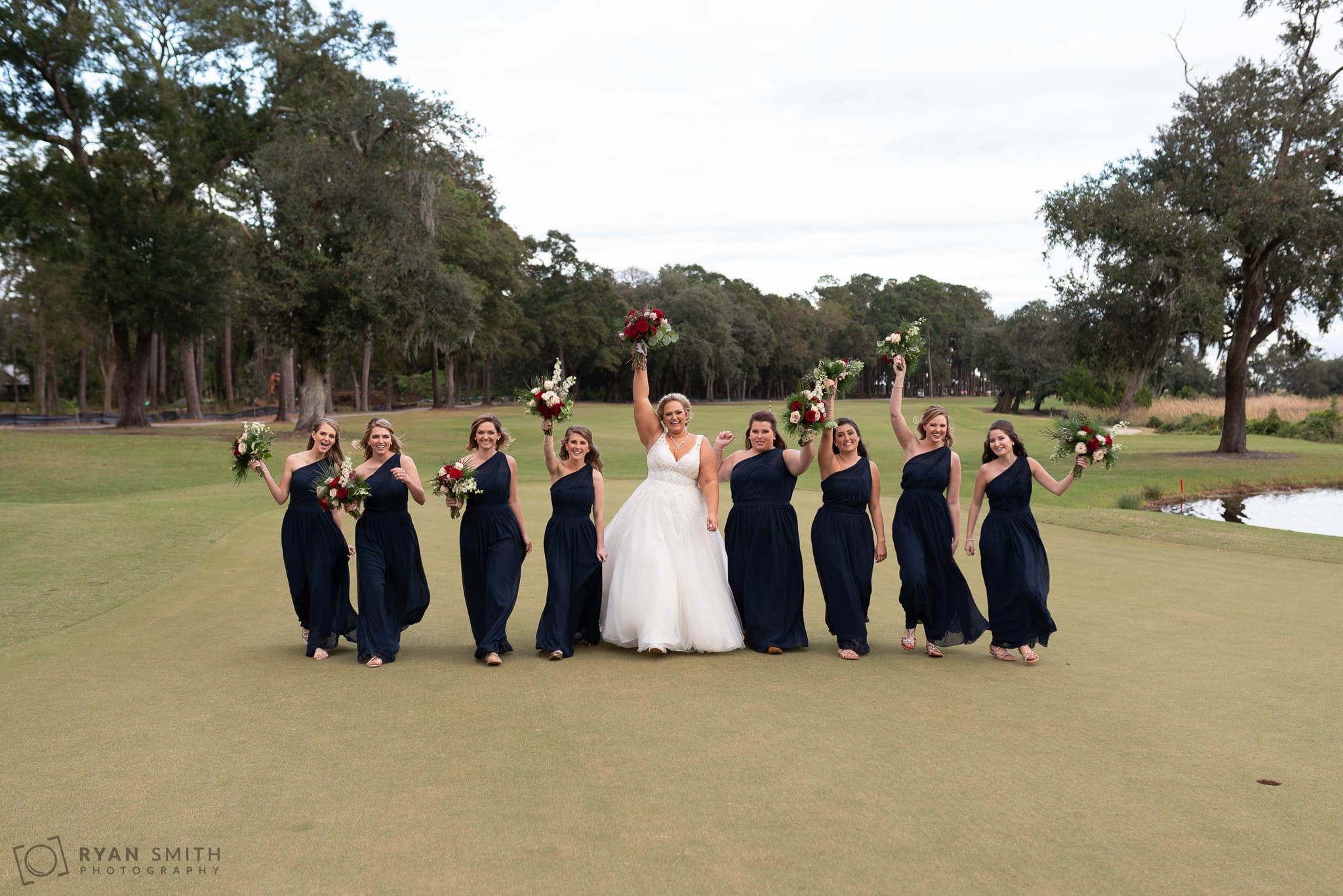 Bridesmaids walking down the green holding flowers in the air