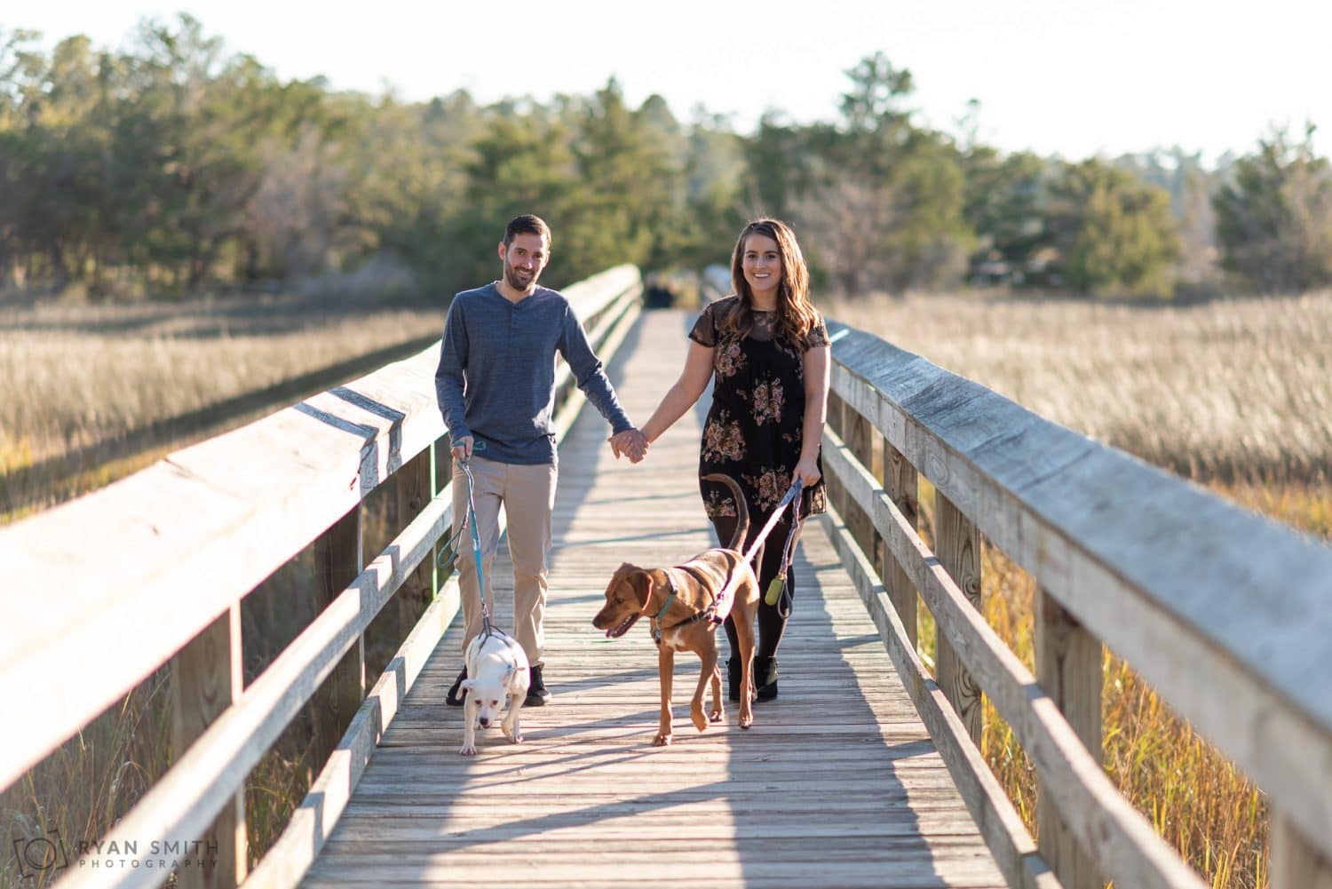 Couple walking down the marsh boardwalk with their dogs Vereen Memorial Gardens