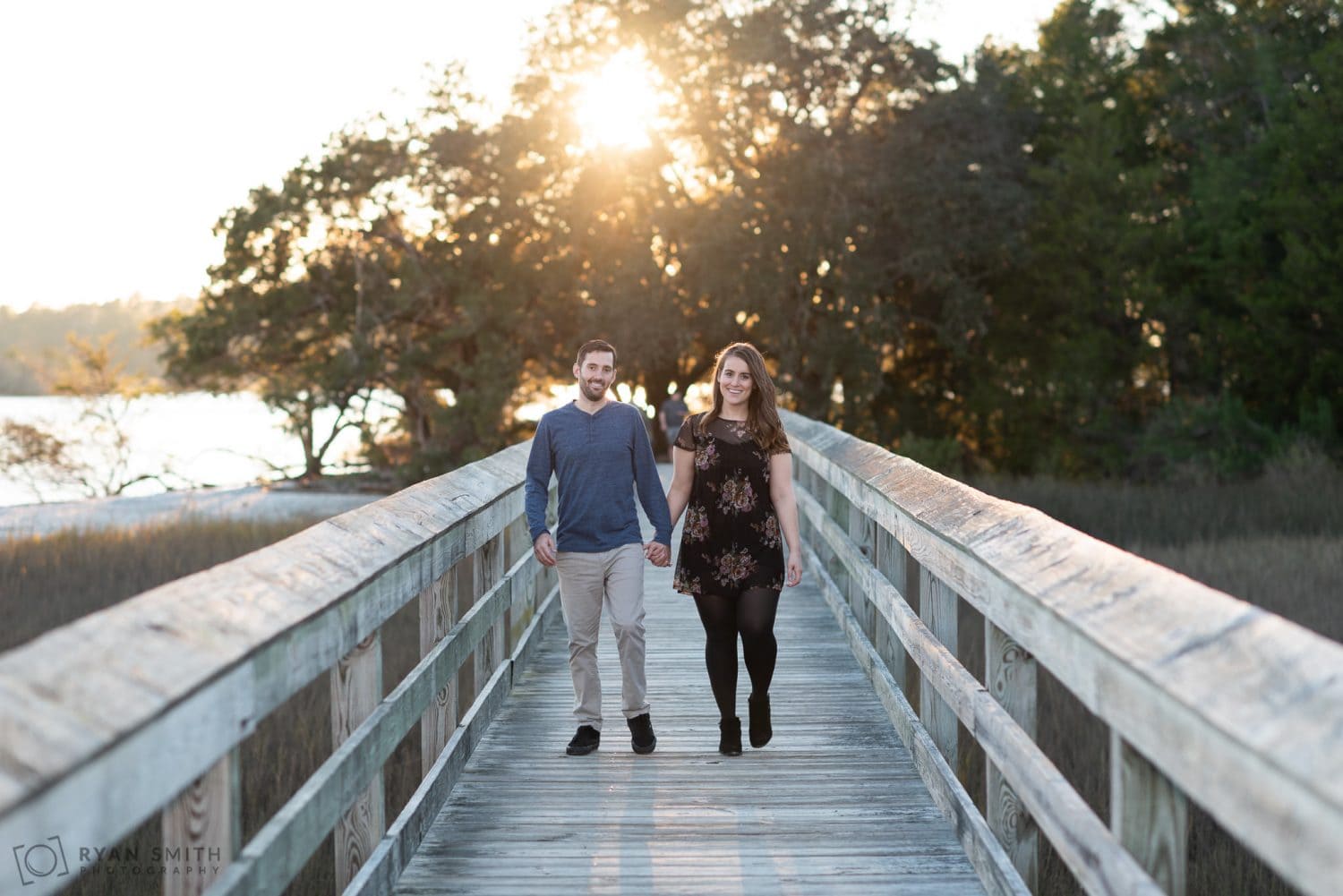 Holding hands walking down the boardwalk backlit by the sun Vereen Memorial Gardens