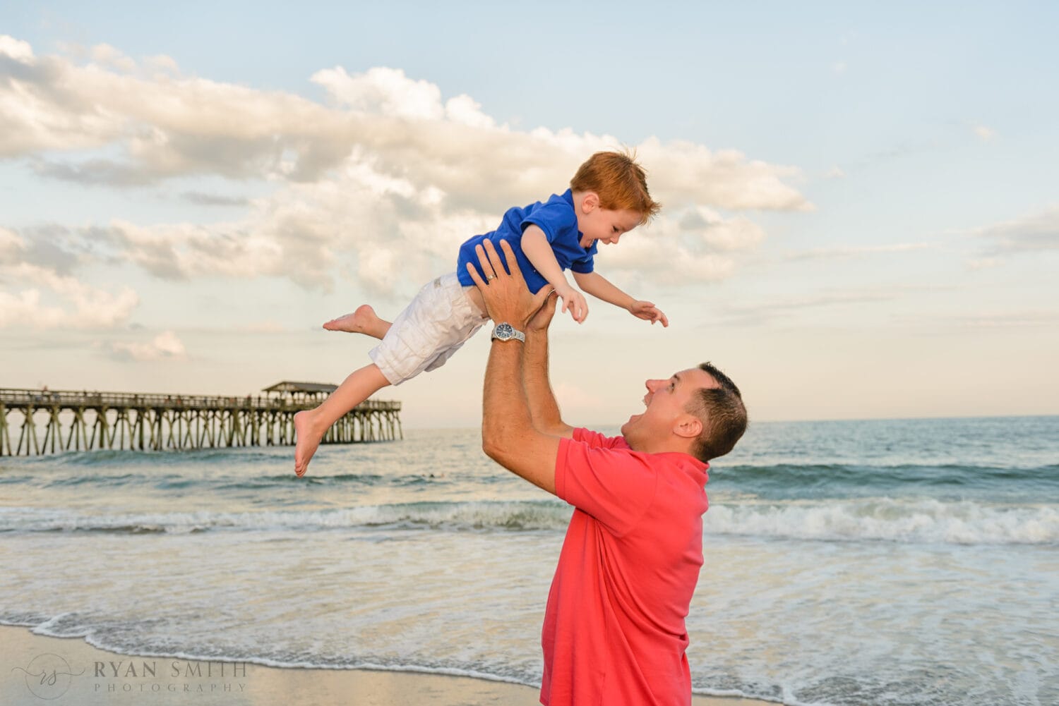 Dad lifting son into the air in front of the pier - Myrtle Beach State Park