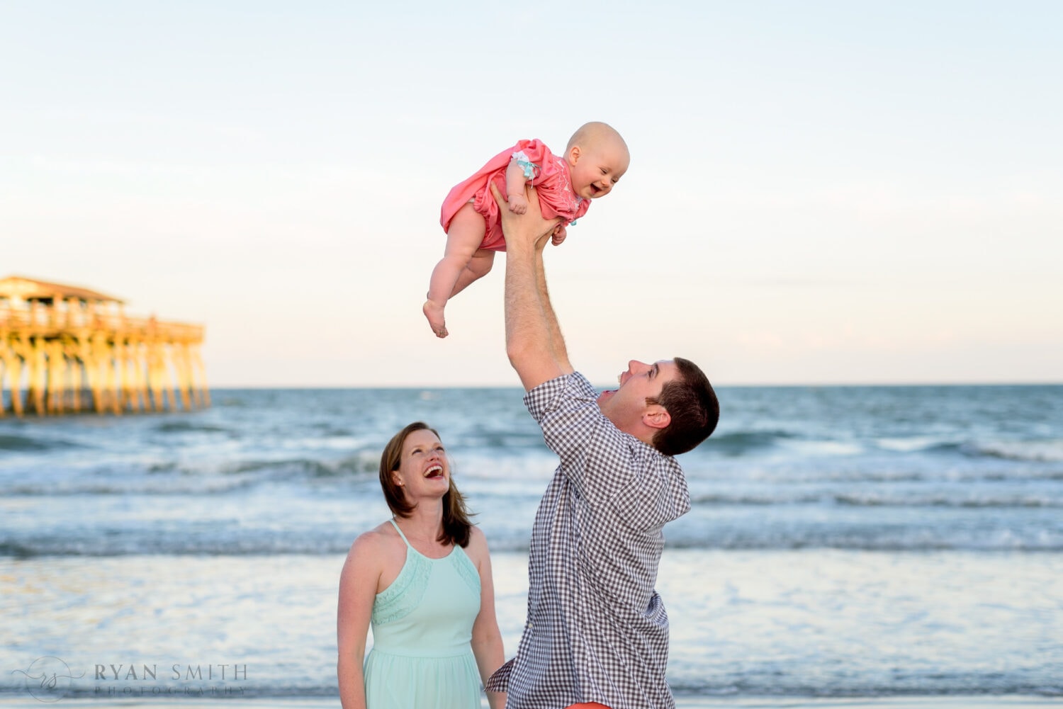 Family of three holding baby in the air in front of ocean - Myrtle Beach State Park
