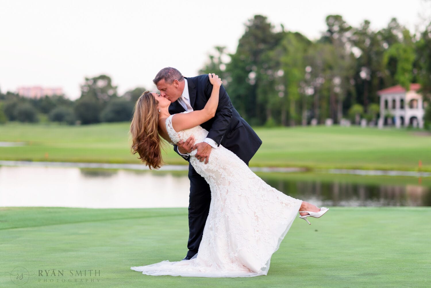 Groom dipping back bride for a kiss on the golf course - Members Club at Grande Dunes