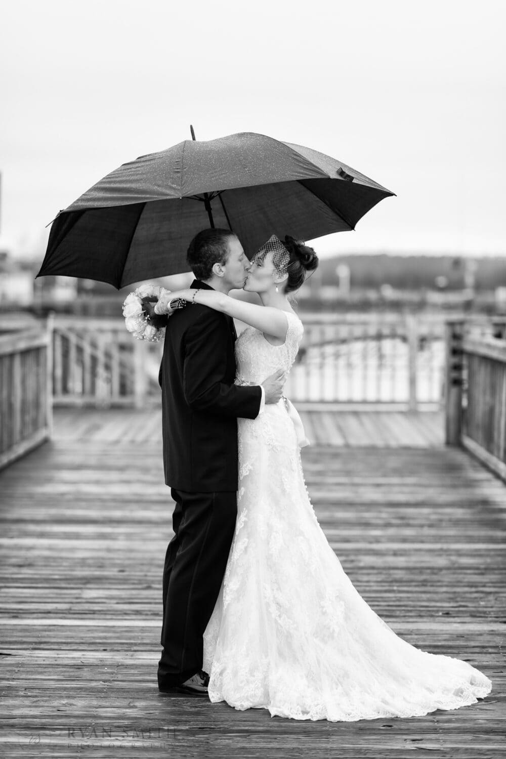 Wedding couple kissing in the rain under an umbrella - Broadway at the Beach