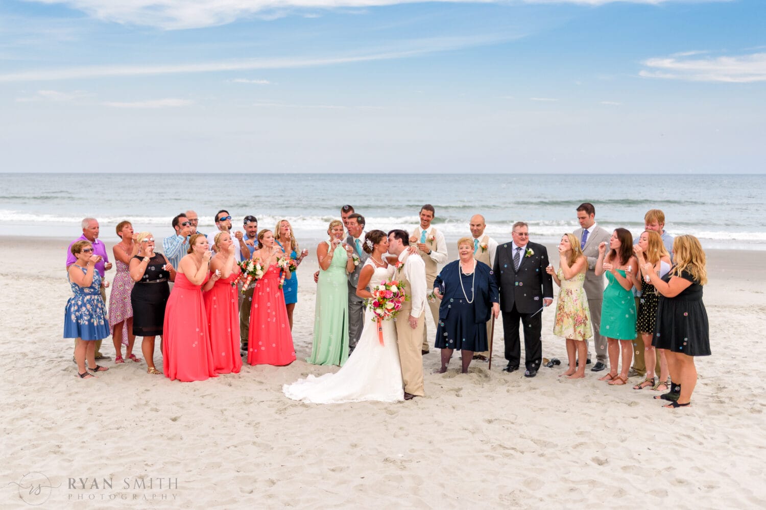 Wedding group blowing bubbles at couple white they kiss - Grande Dunes Ocean Club