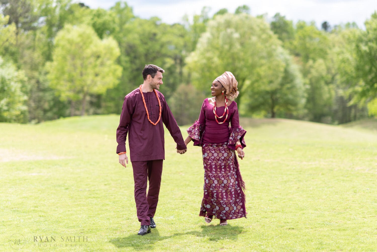 Couple holding hands walking down the golf course in traditional African wedding dress - River Ridge Golf Club