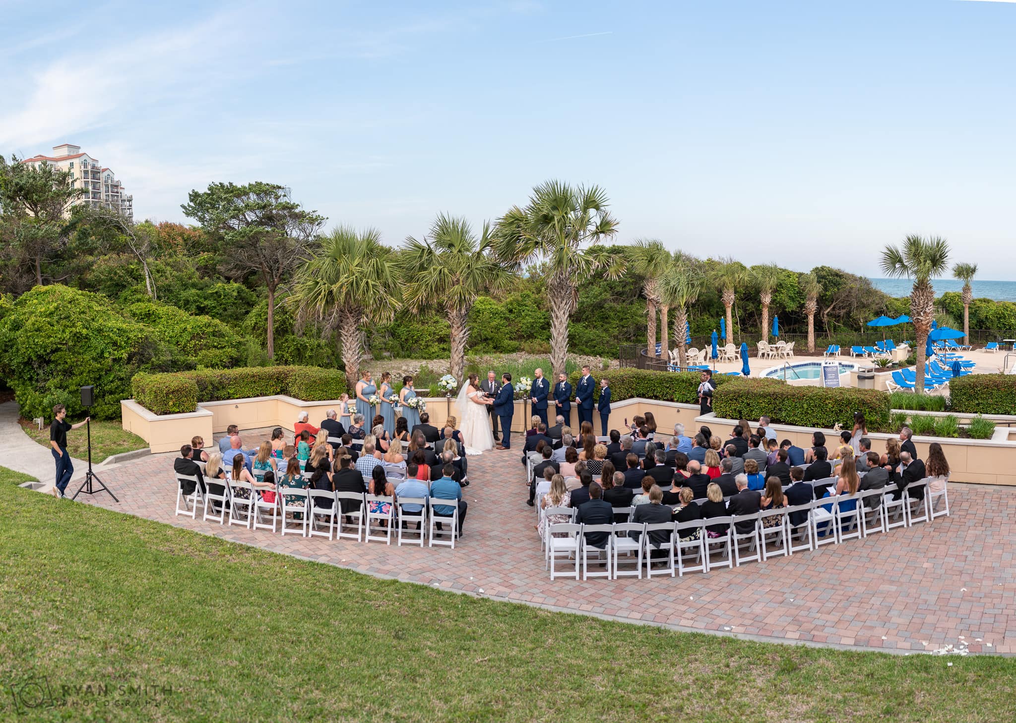Panorama of wedding ceremony by the palm trees and pool Grande Dunes Ocean Club