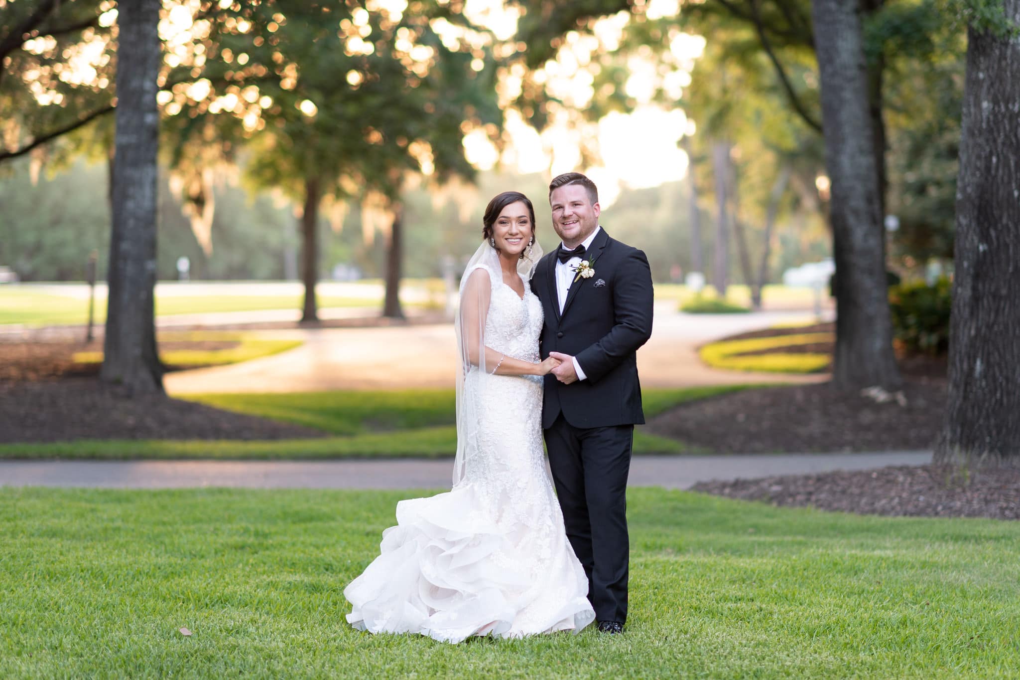 Bride and groom smiling at camera with sunset filtering through the trees Pawleys Plantation