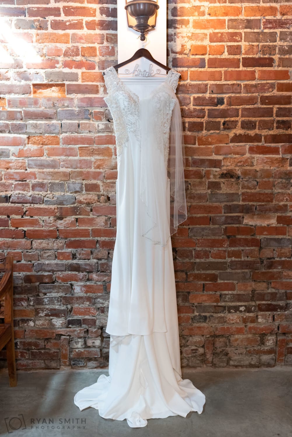 Bride's dress hanging on the brick wall - Hennigan Salon - Conway