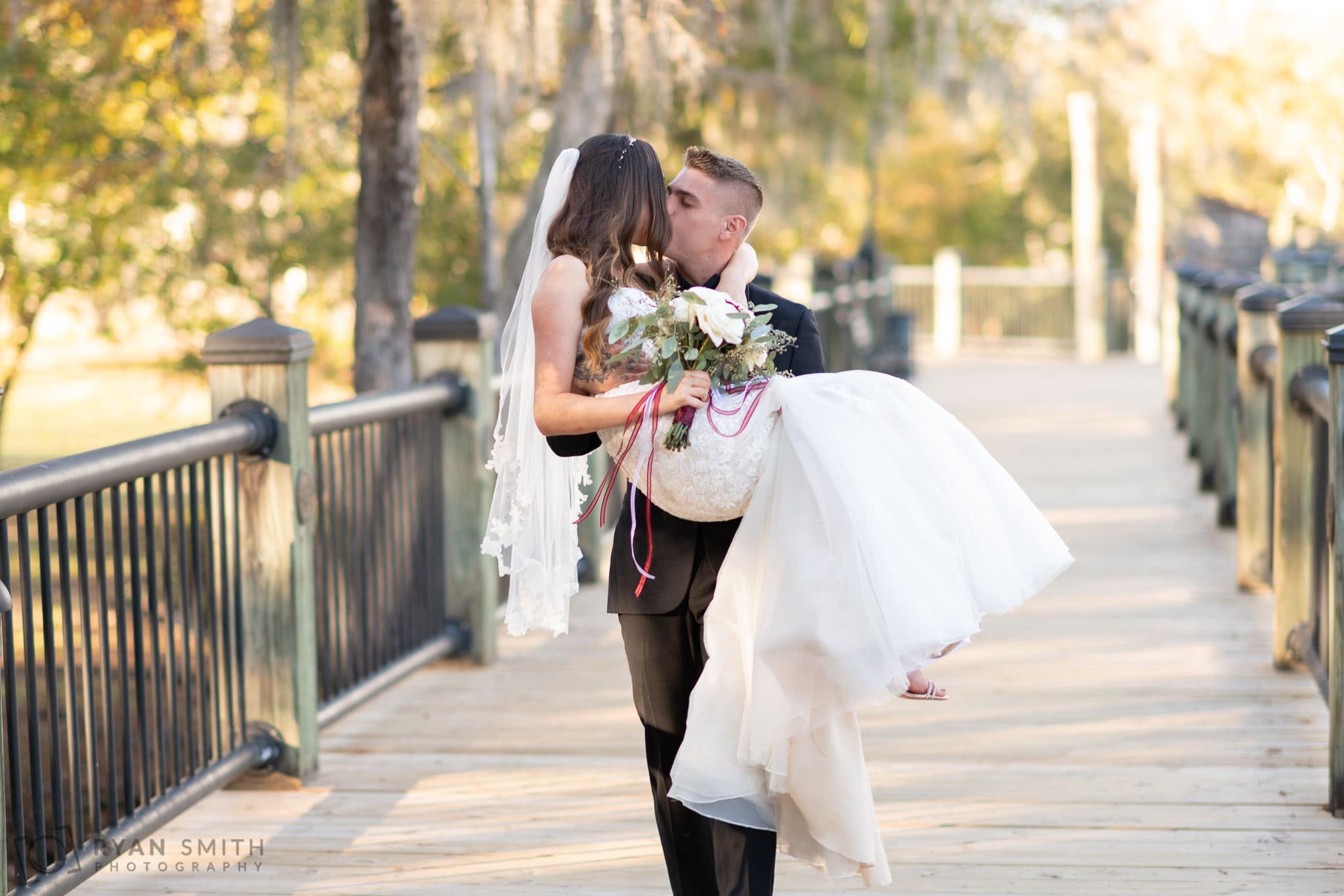 Groom carrying bride down the boardwalk - Conway River Walk