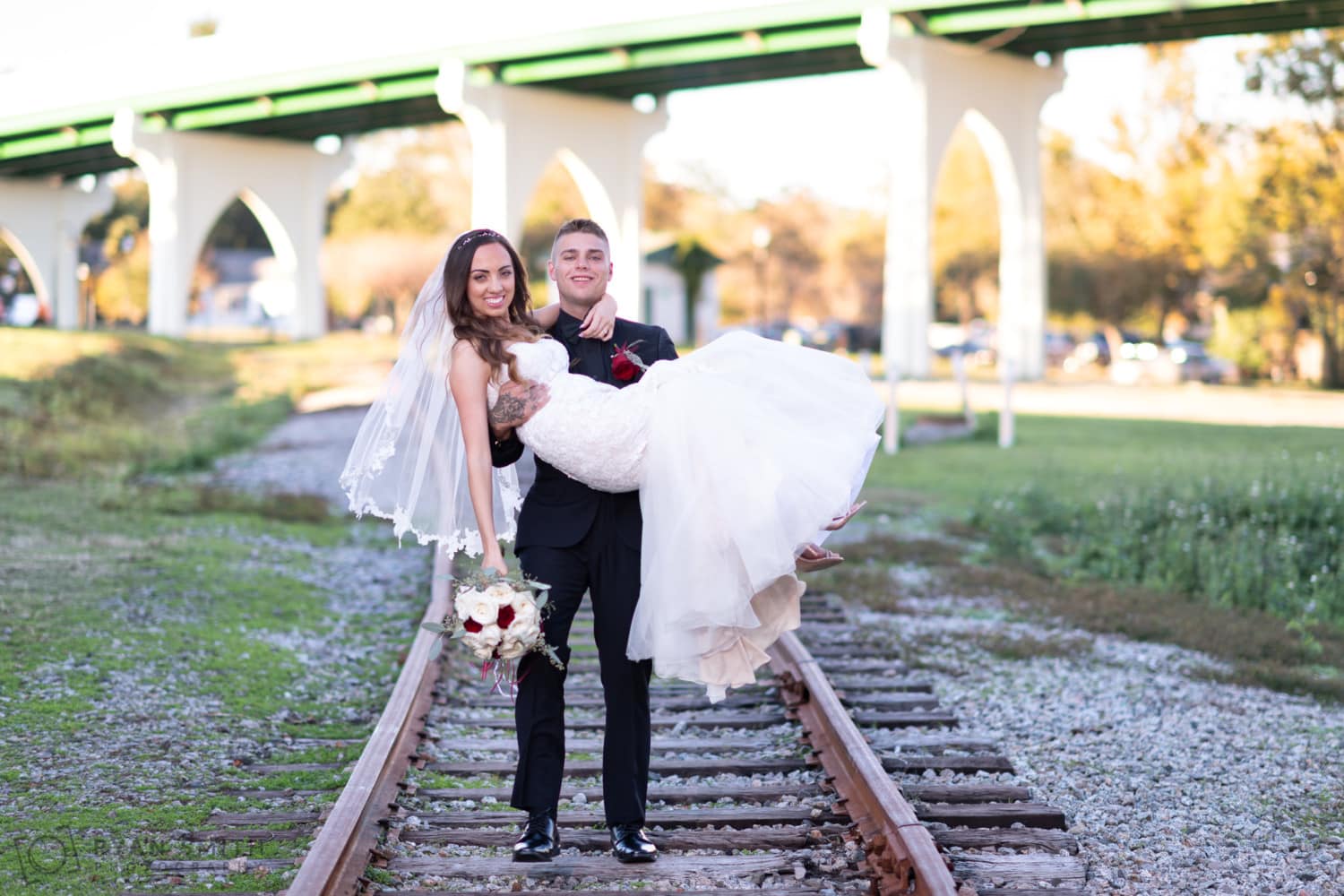 Groom carrying bride to the ceremony down the train tracks -