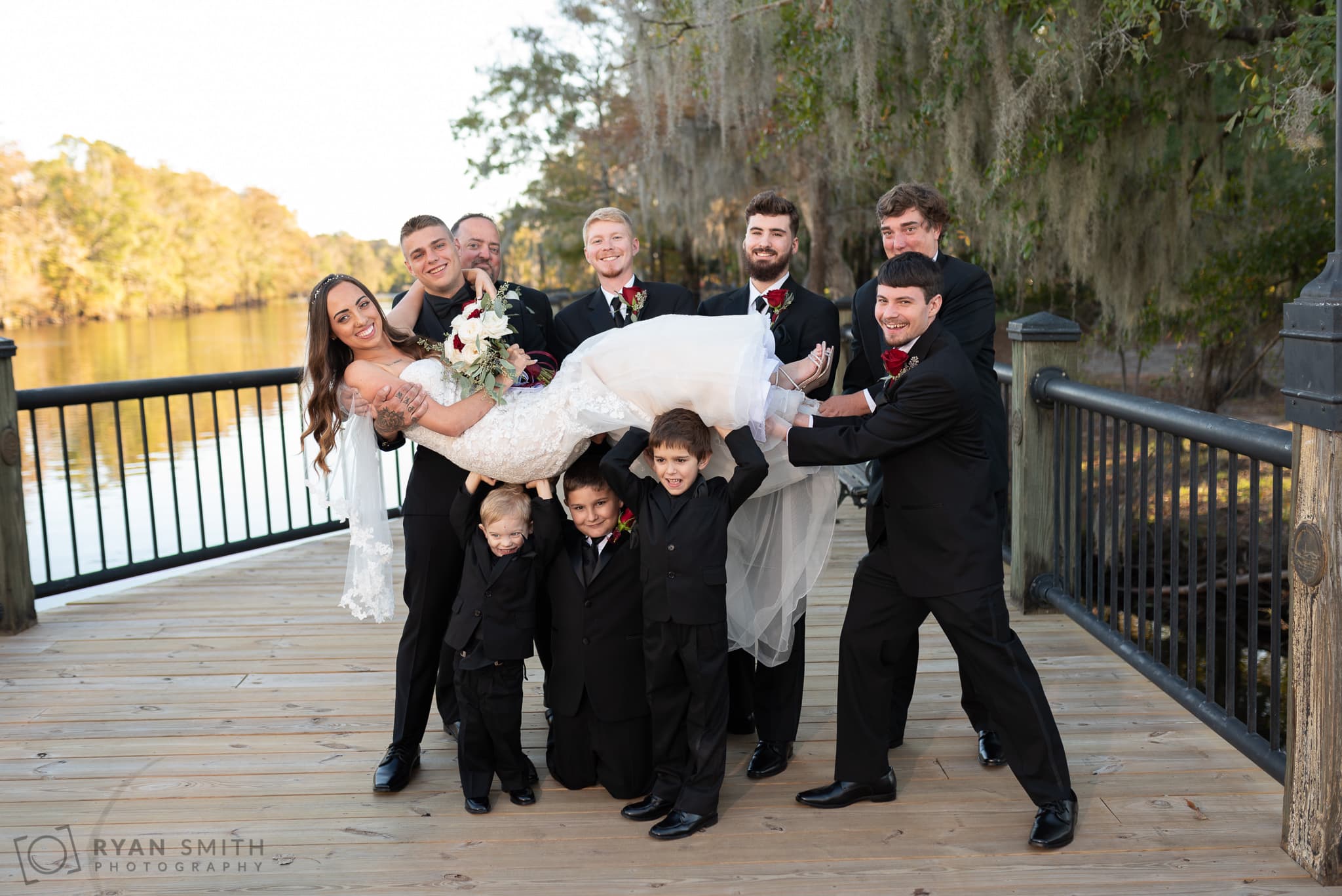 Groomsmen and kids lifting up the bride into the air - Conway River Walk