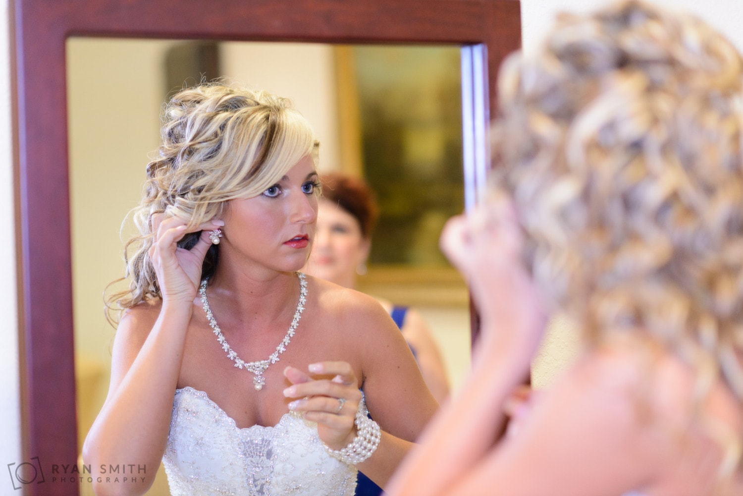 Bride putting on earrings in the mirror - Members Club at Grande Dunes