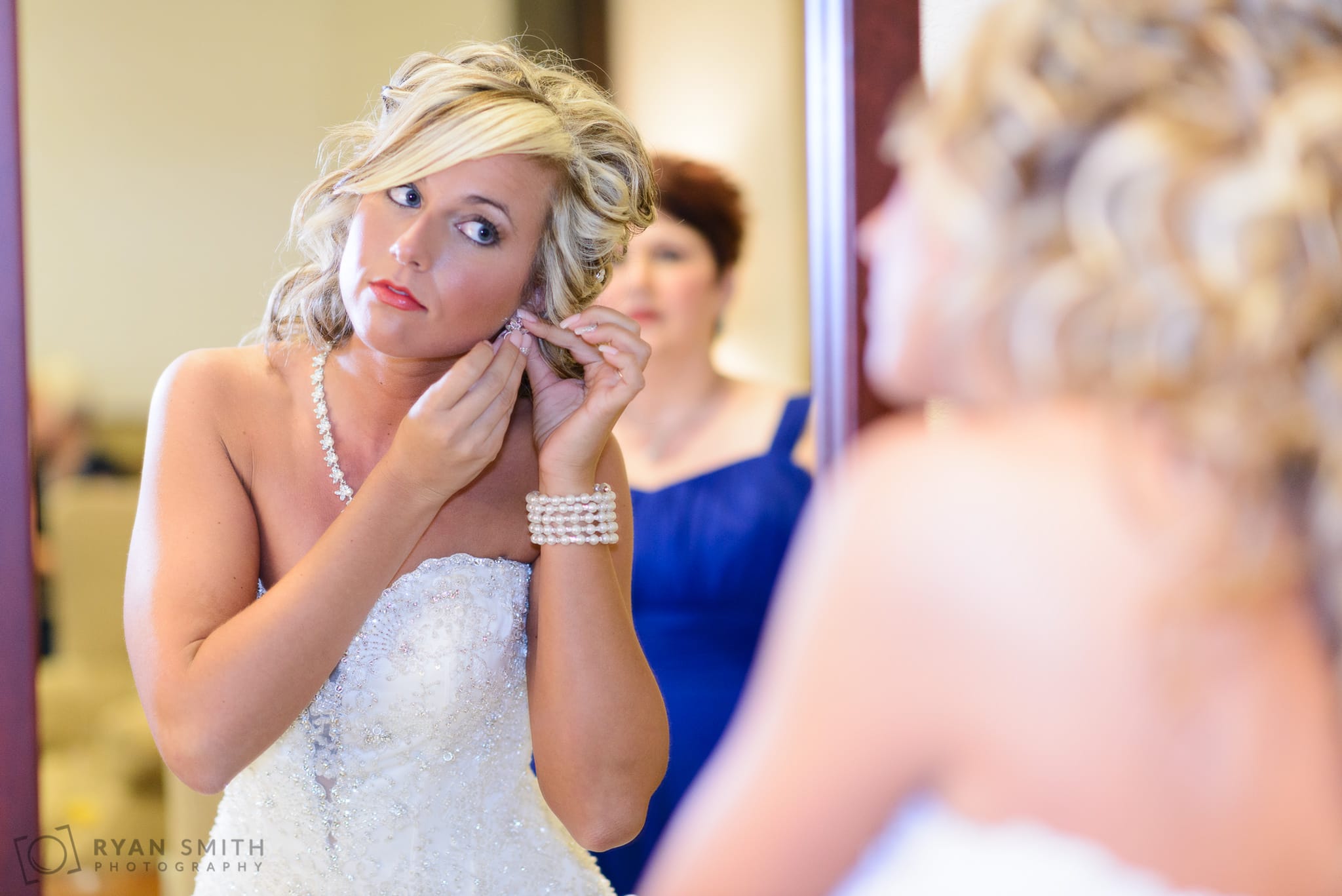 Bride putting on earrings in the mirror - Members Club at Grande Dunes