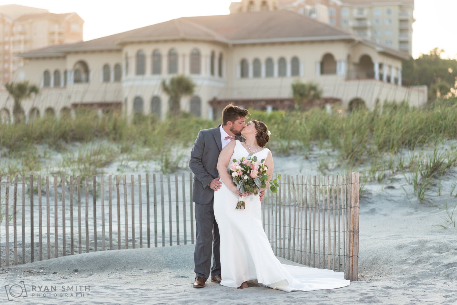 Bride and groom with sunset and clubhouse in the background - Grande Dunes Ocean Club - Myrtle Beach