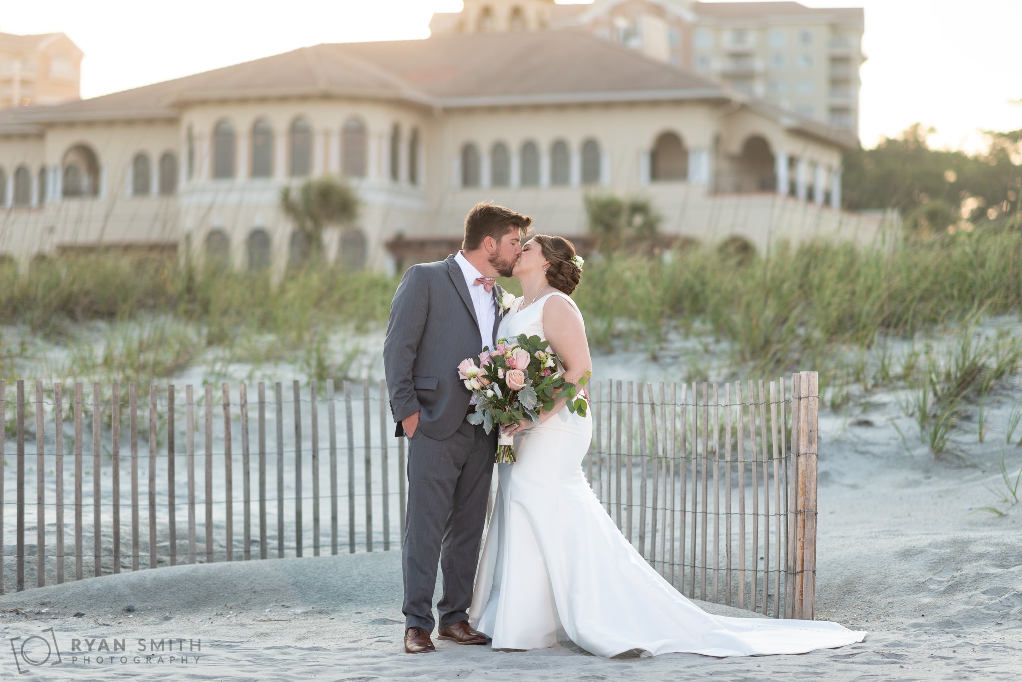 Bride and groom with sunset and clubhouse in the background - Grande Dunes Ocean Club - Myrtle Beach
