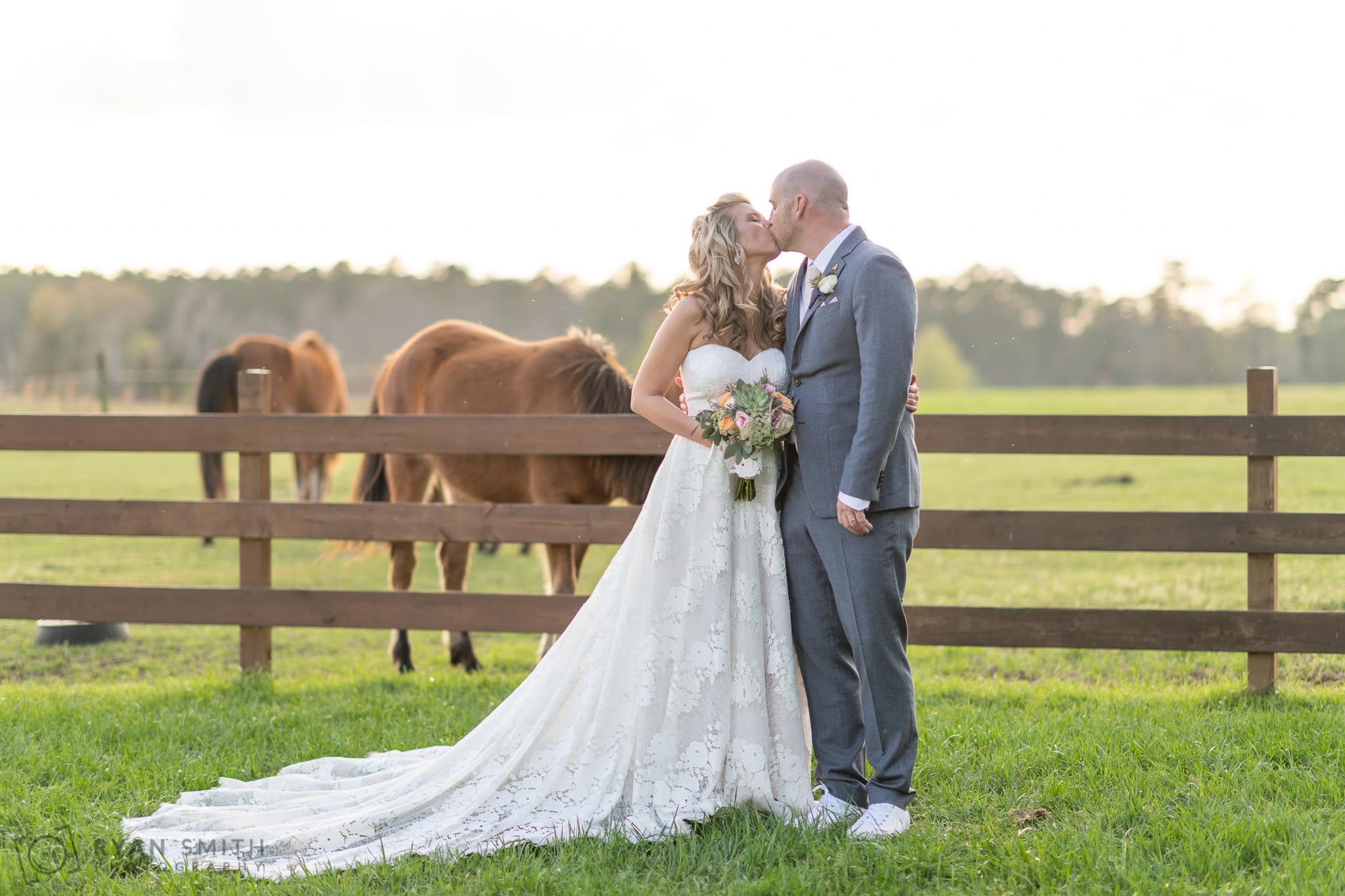 Bride and groom kissing with horses in the background - Wildhorse at Parker Farms