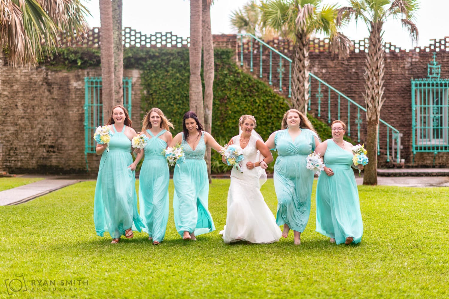 Bridesmaids skipping together with arms linked  - Atalaya Castle - Huntington Beach State Park