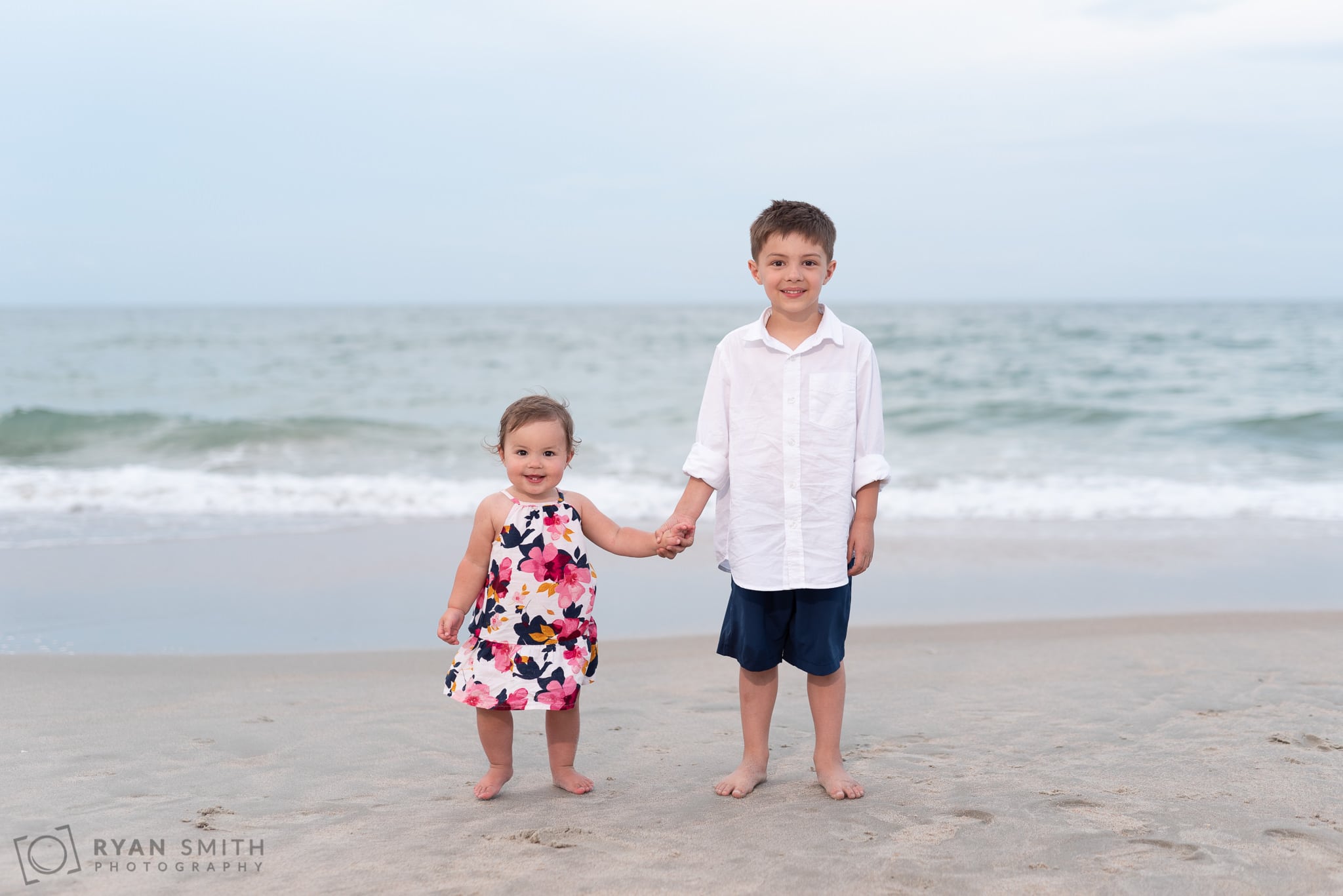 Little brother and sister holding hands in front of the ocean - Huntington Beach State Park