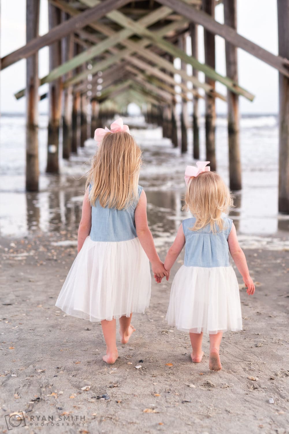 Sisters holding hands walking under the pier - Ocean Isle
