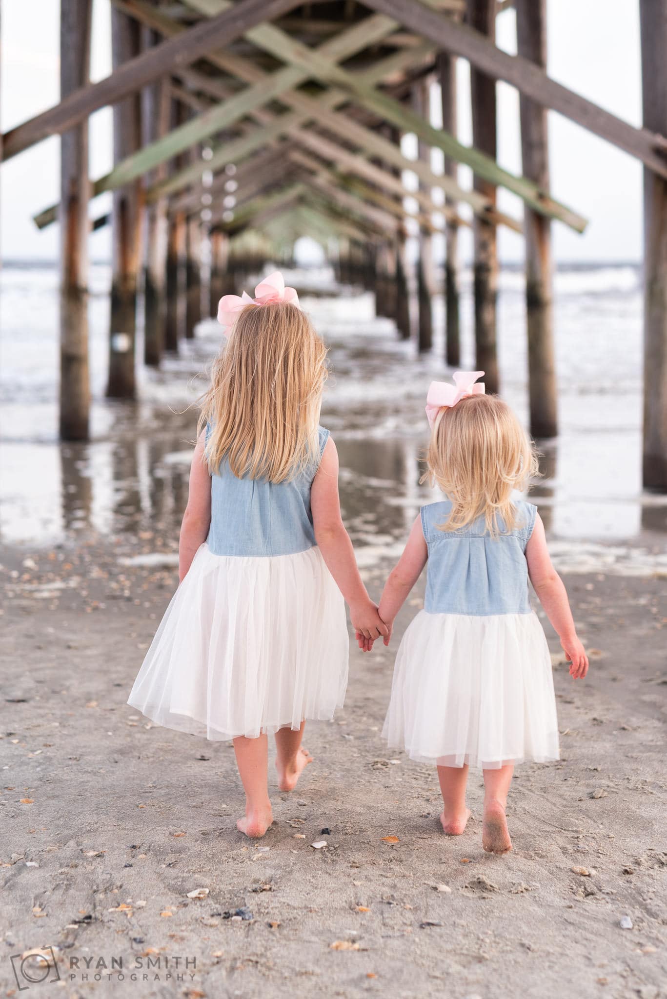 Sisters holding hands walking under the pier - Ocean Isle