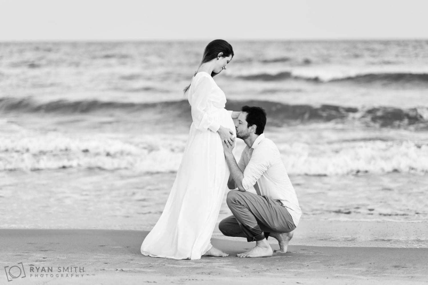 Black and white portraits of husband and expecting mother in front of the ocean - Huntington Beach State Park