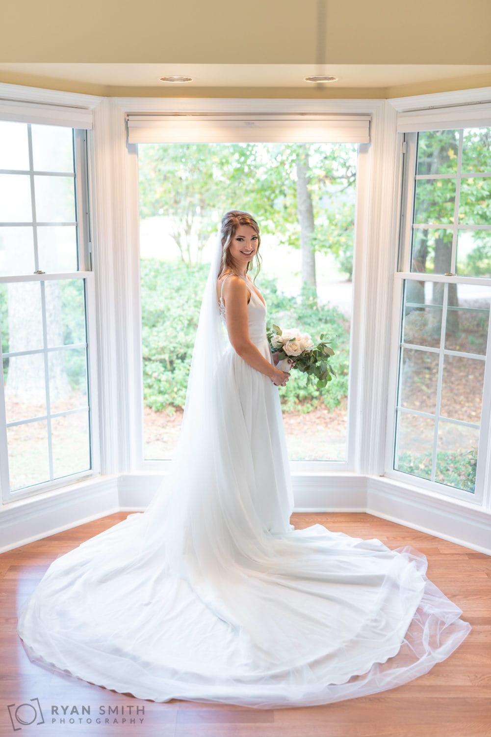 Bride standing in the windows overlooking the golf course - Wachesaw Plantation