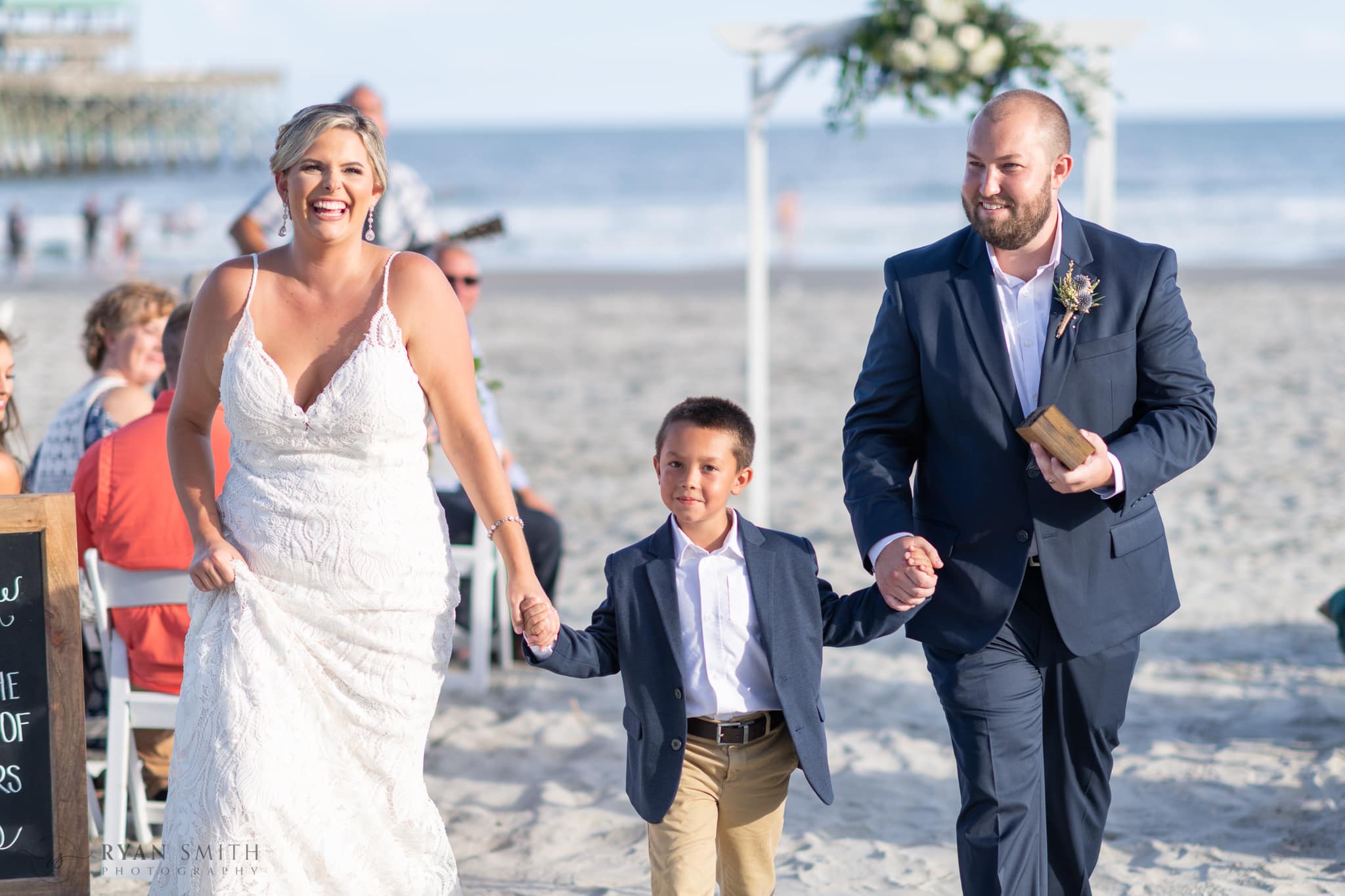 Bride and groom walking from ceremony with son - Folly Beach - Charleston