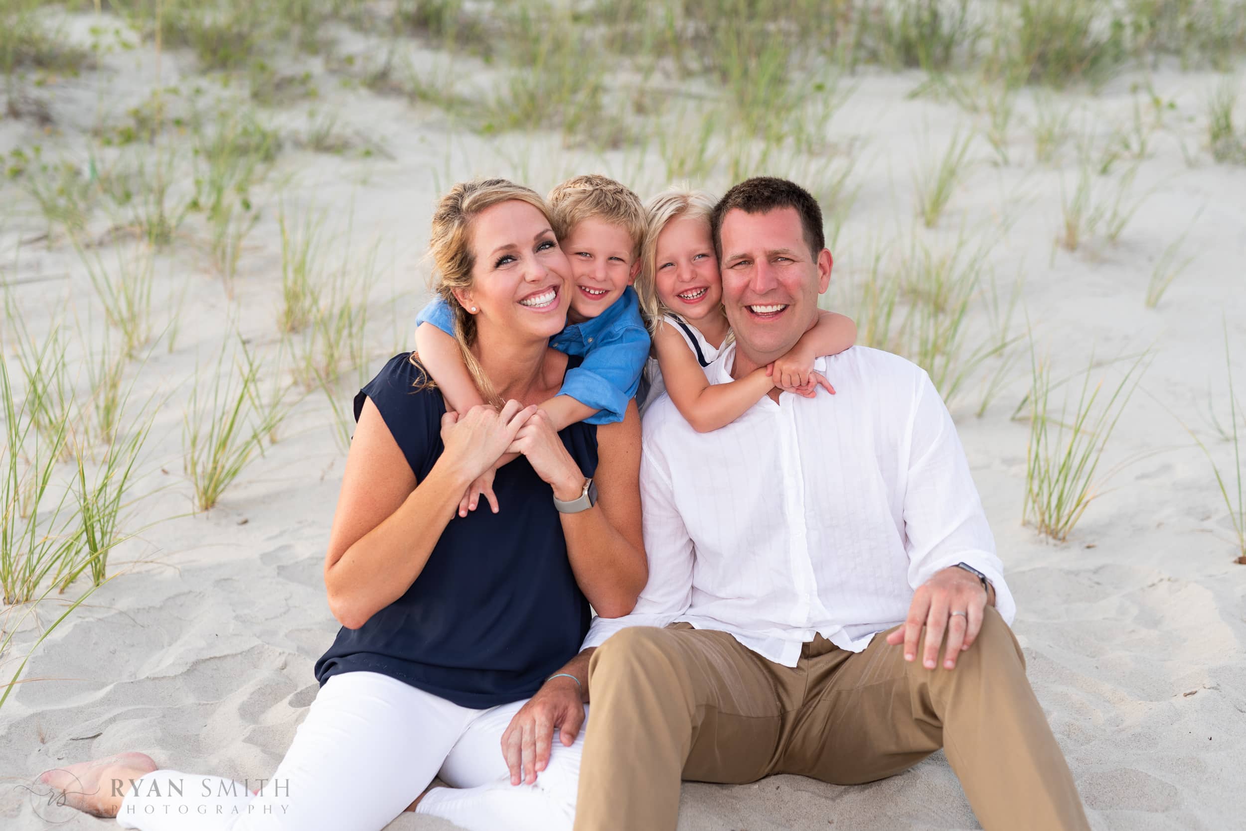 Happy family of 4 in Ocean Isle sitting by the dunes -