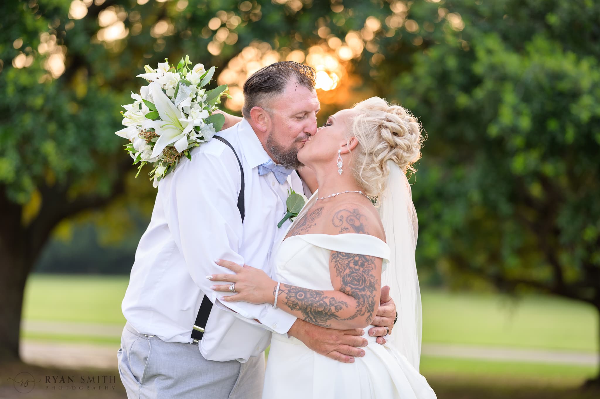 Kiss holding flowers behind groom neck  - Wild Wing Plantation