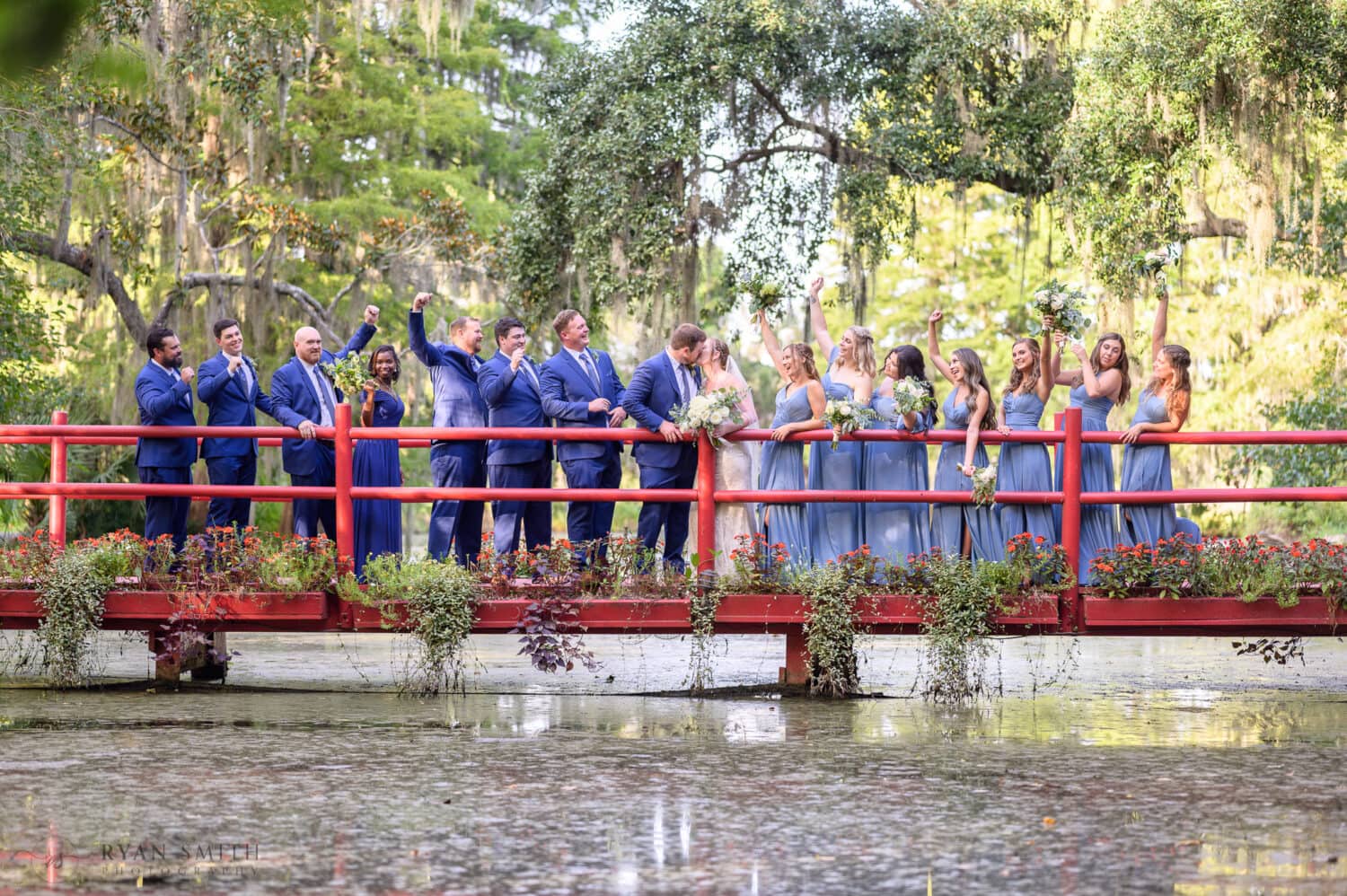 Kiss with bridal party cheering on the red bridge - Magnolia Plantation