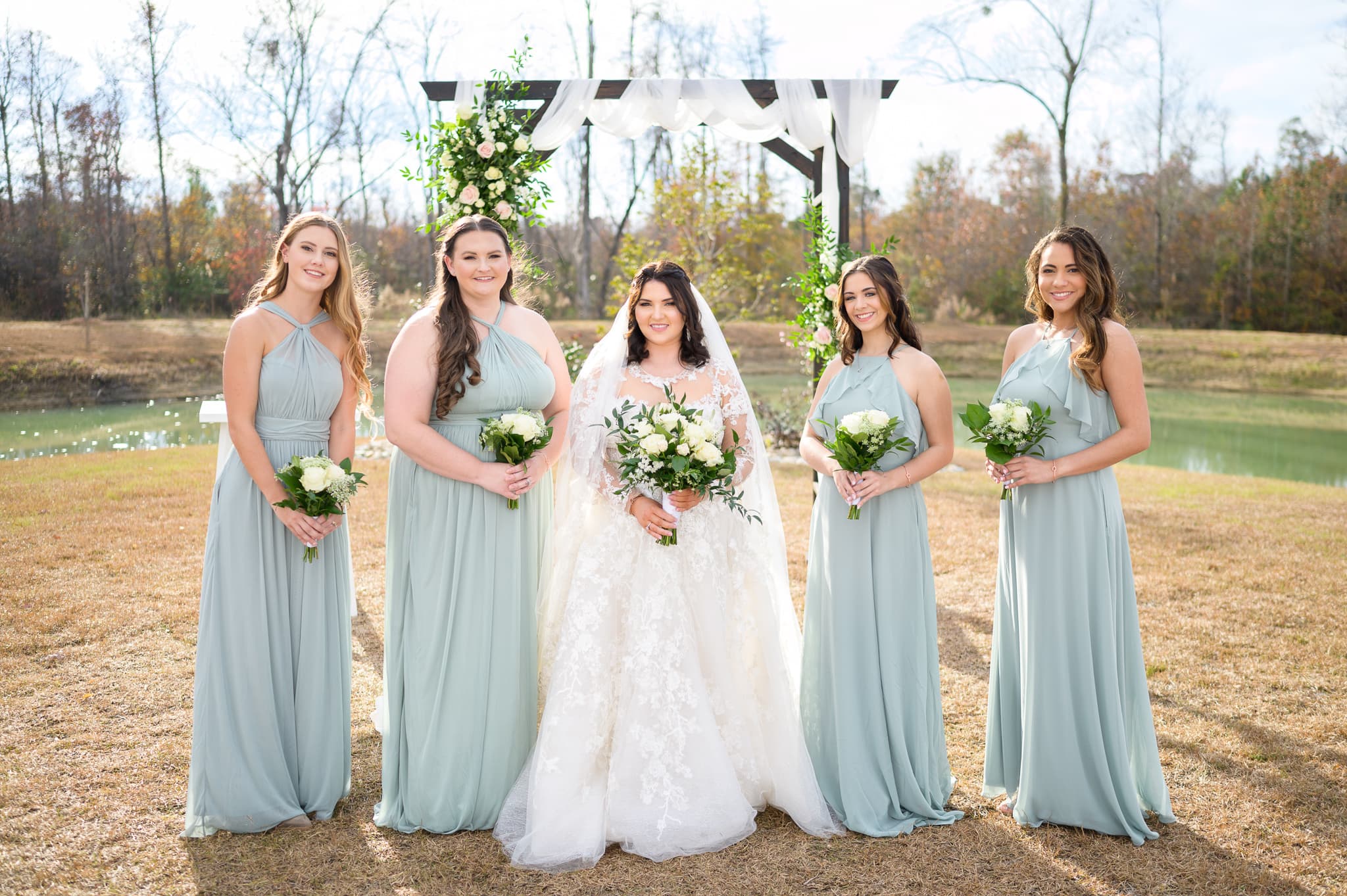 Bride with bridesmaids in front of wedding arch - The Venue at White Oaks Farm