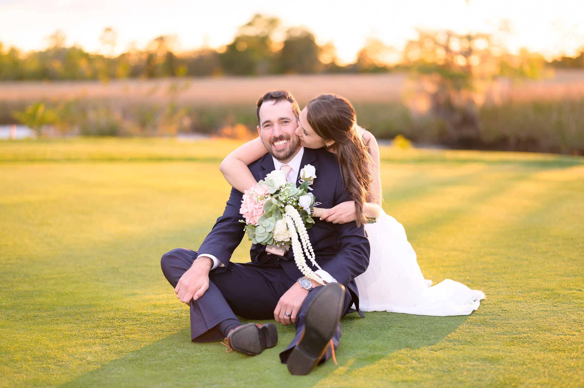 Bride hugging groom from behind sitting on the golf course - Caledonia Golf & Fish Club