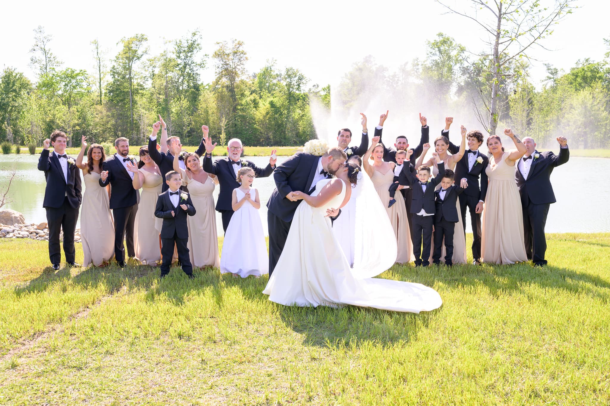 Bride and groom kissing with cheering bridal party in background - The Venue at White Oaks Farm