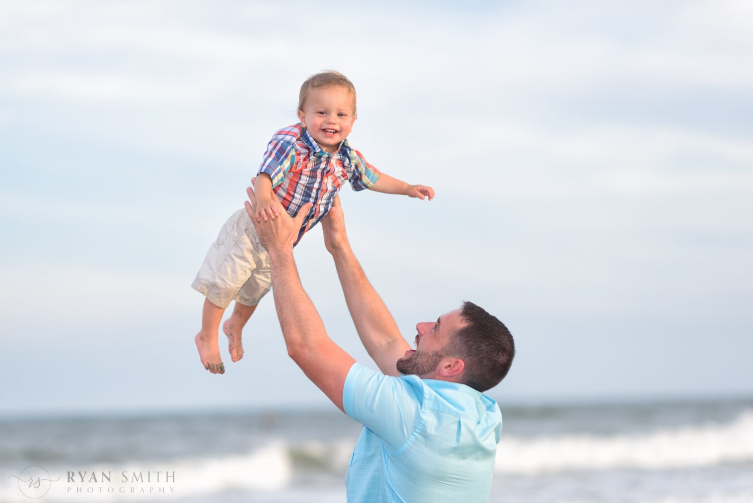 Dad tossing son in the air smiling at the camera - Myrtle Beach State Park