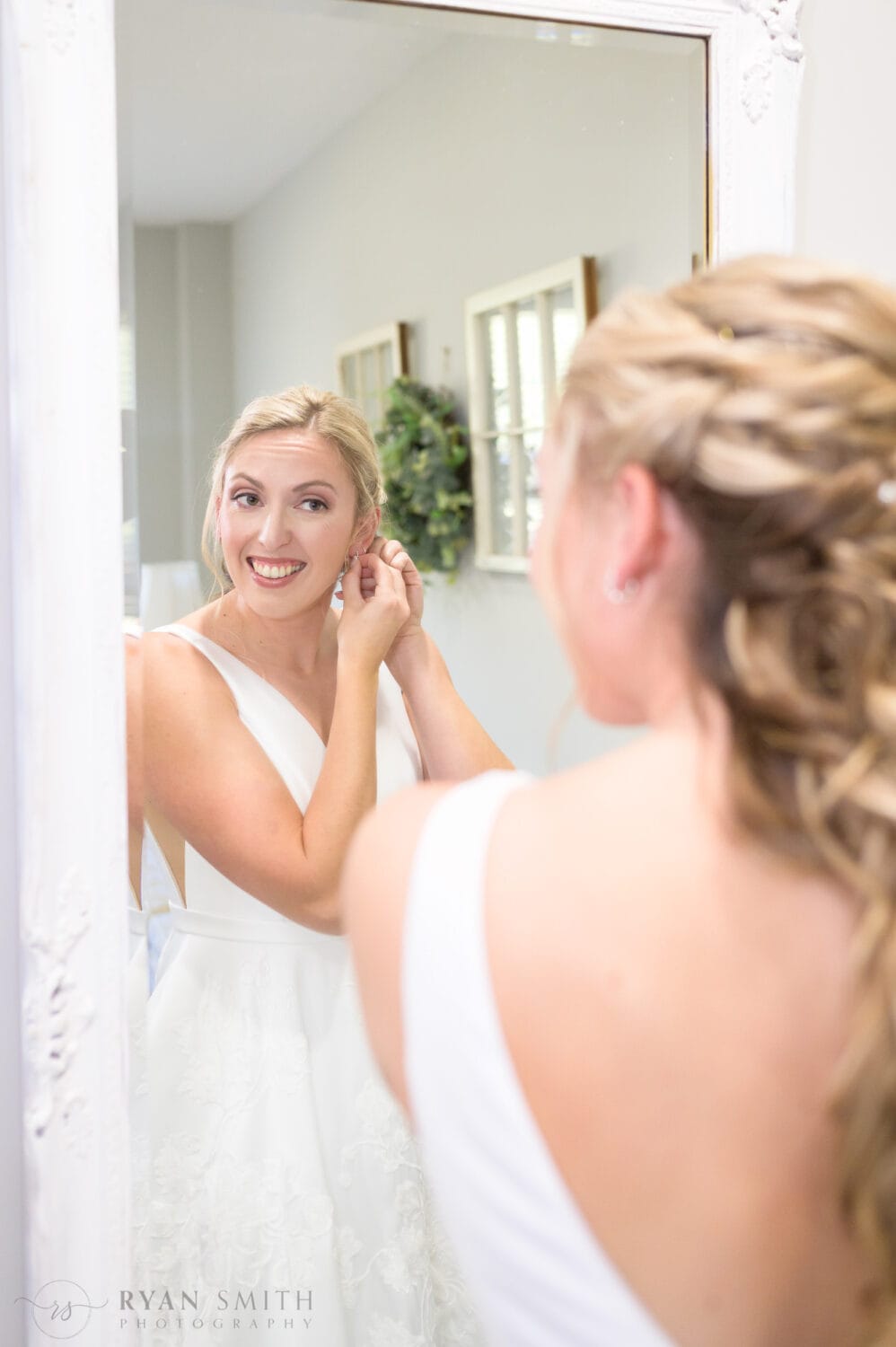 Bride putting on earrings in the mirror - The Blessed Barn