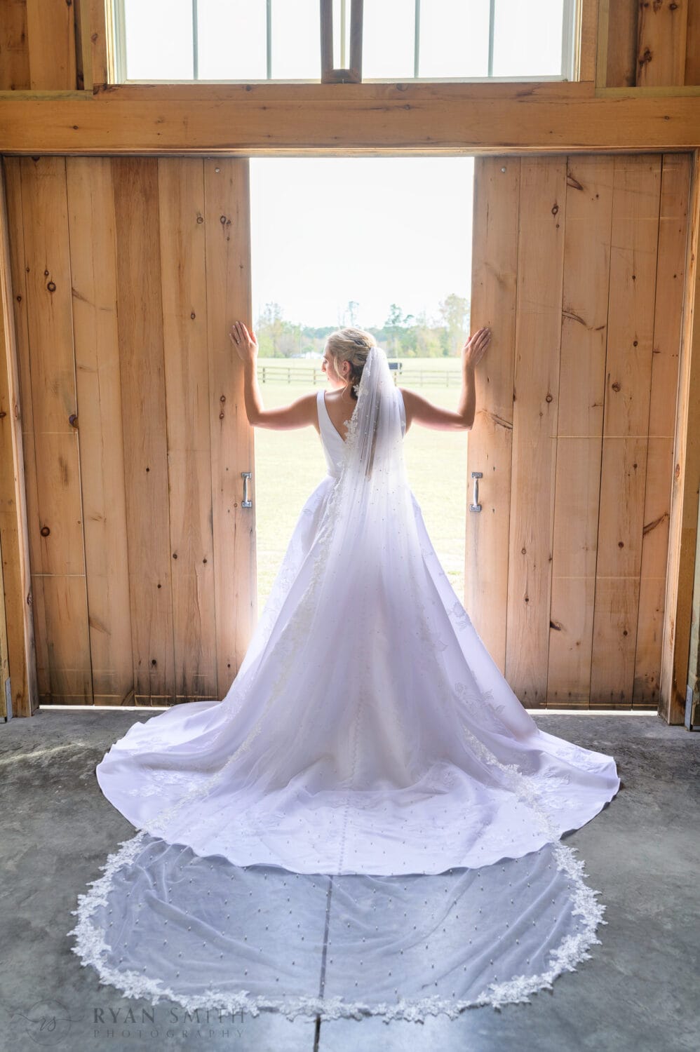 Bride standing in the light coming through the barn doors - The Blessed Barn