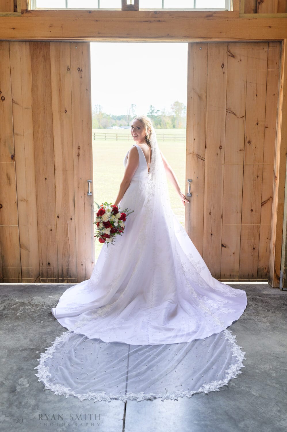 Bride standing in the light coming through the barn doors - The Blessed Barn