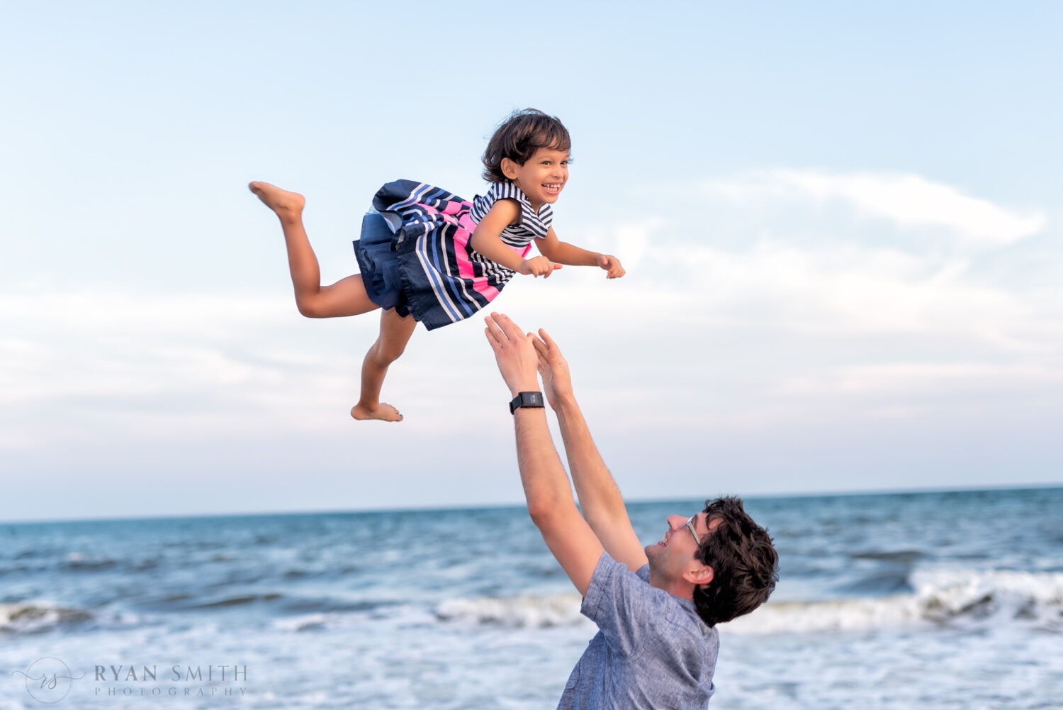 Dad tossing daughter into the air in front of the ocean -