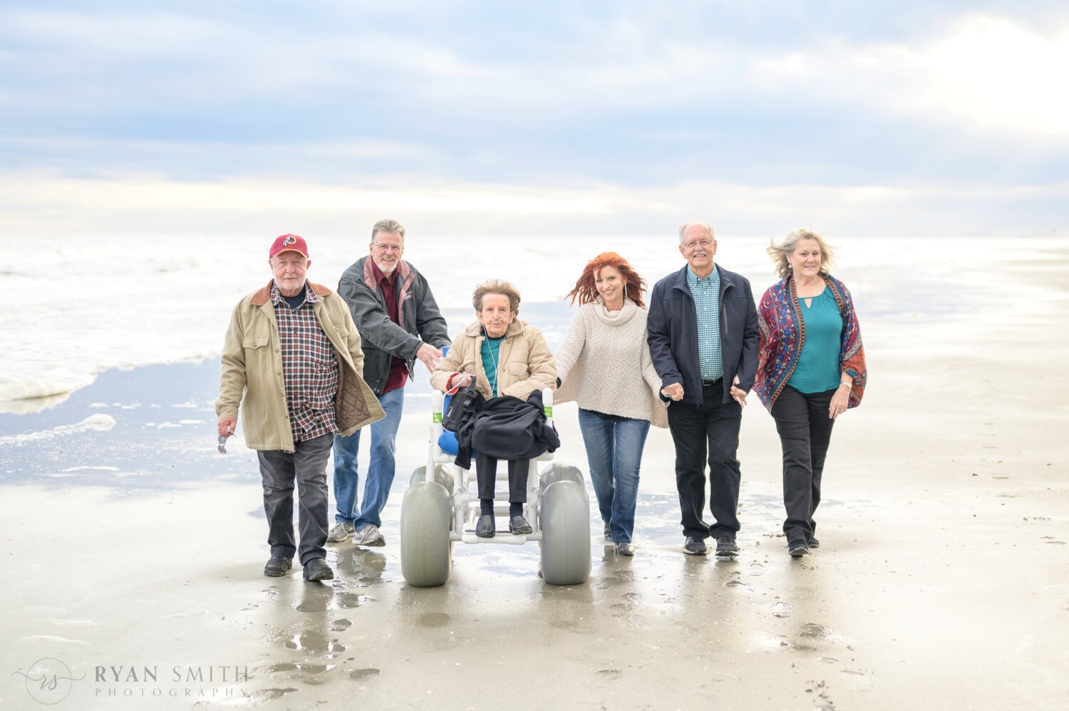 Family with mother in beach wheelchair walking by the ocean - North Myrtle Beach