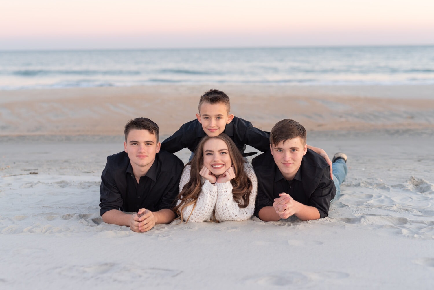 Little brother laying on top of siblings in the sand -