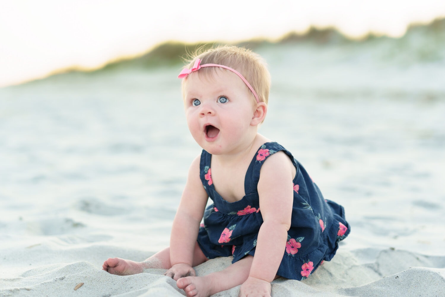 Baby girl with big blue eyes sitting by the ocean -